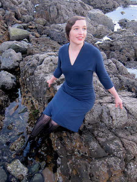 Leimomi, a white woman with her hair in a braid, is shown wearing the Scroop Miramar Dress with 3/4 length sleeves in slate blue wool knit