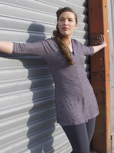 Leimomi, a white woman with her hair in a braid, is shown wearing the Scroop Miramar Tunc with 3/4 sleeves in purple jacquard merino viscose knit.