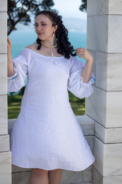 Woman in a white 17th c shift standing in front of a stone wall with a scenic background