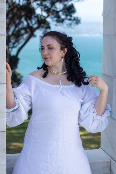 Woman in a white 17th c shift standing outdoors with a scenic background