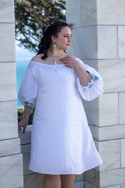 Woman in a white 17th c shift standing against a stone wall with ocean view