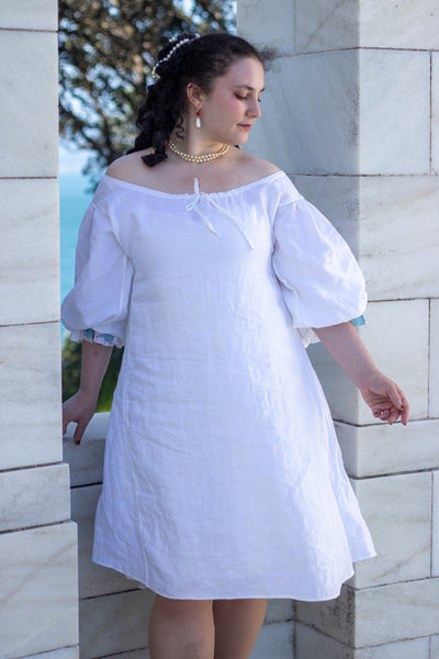 Woman wearing a white 17th c shift with puffed sleeves against a stone wall.