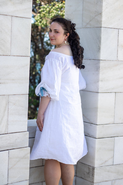 Woman in a white 17th c shift standing against a stone wall with trees in the background