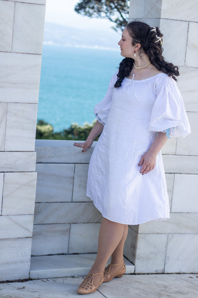 Woman in a white 17th c shift standing against a stone wall with ocean view