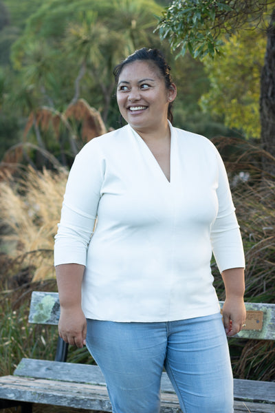 Rose, a Pasifika woman with her hair in a ponytail, is shown wearing the Scroop Miramar Top with 3/4 length sleeves in ivory ponte knit